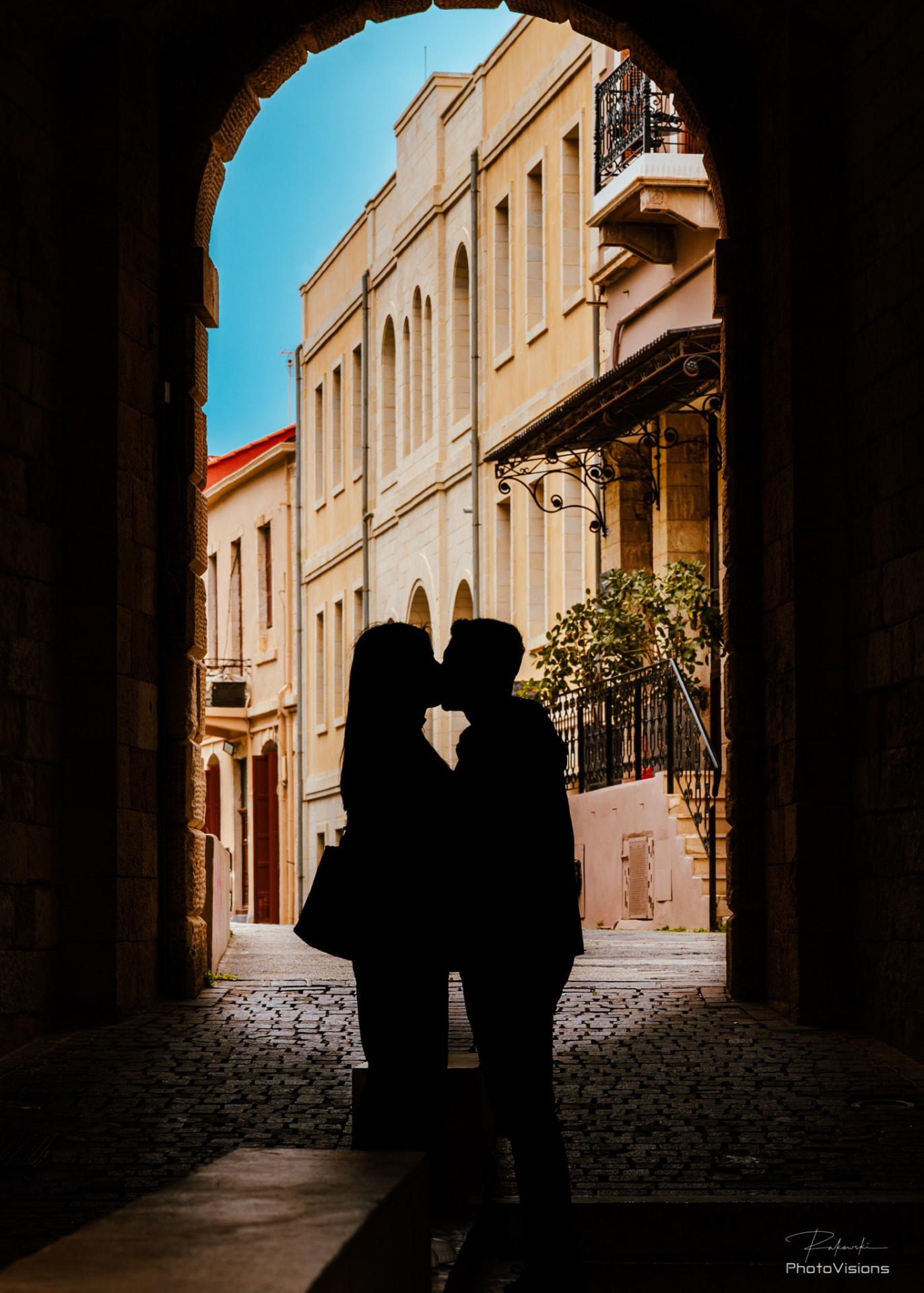 A couple kissing in silhouette beneath a stone archway